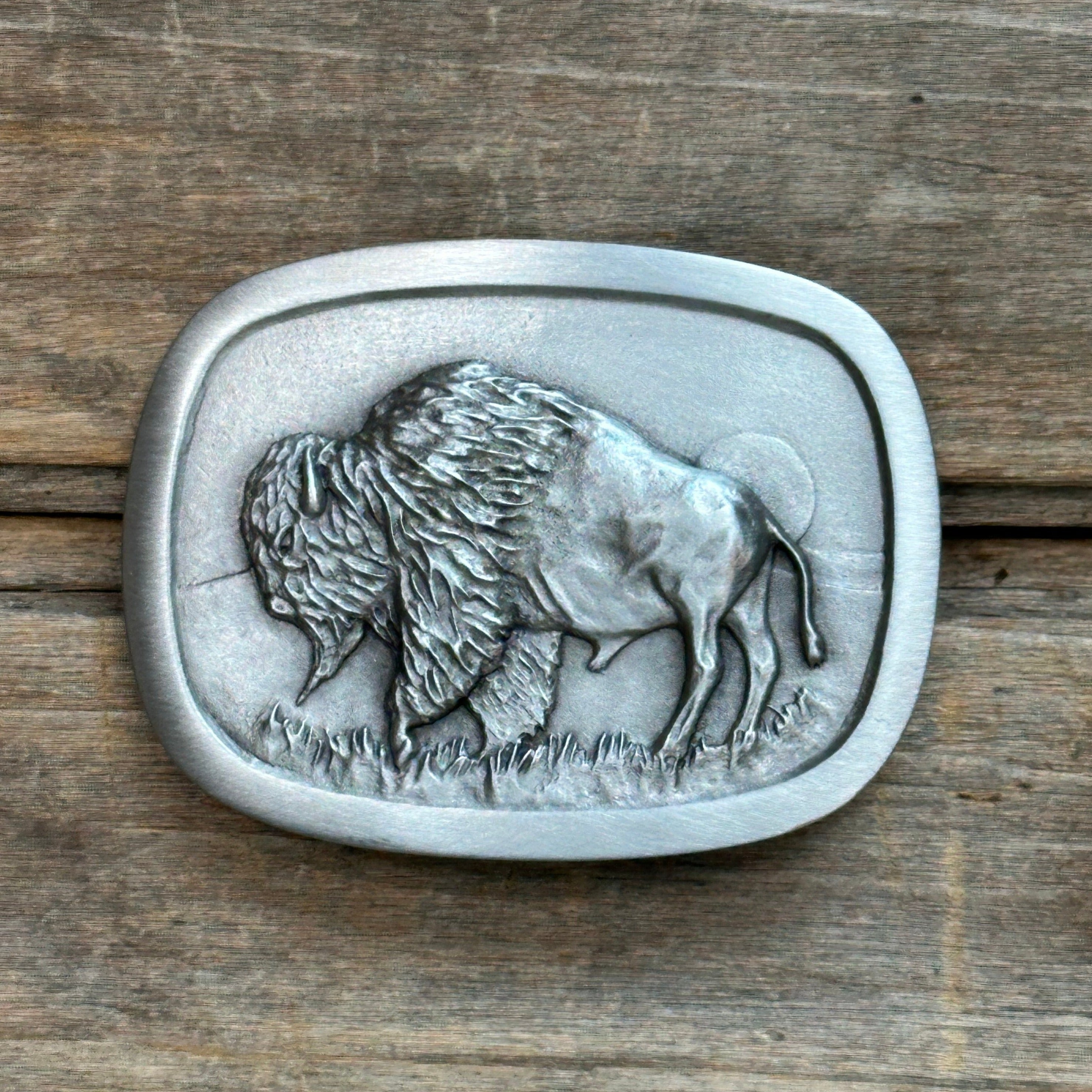 This is a pewter buckle with a silver tone.  It depicts a bison on the prairie with a sun setting over the hills in the background.