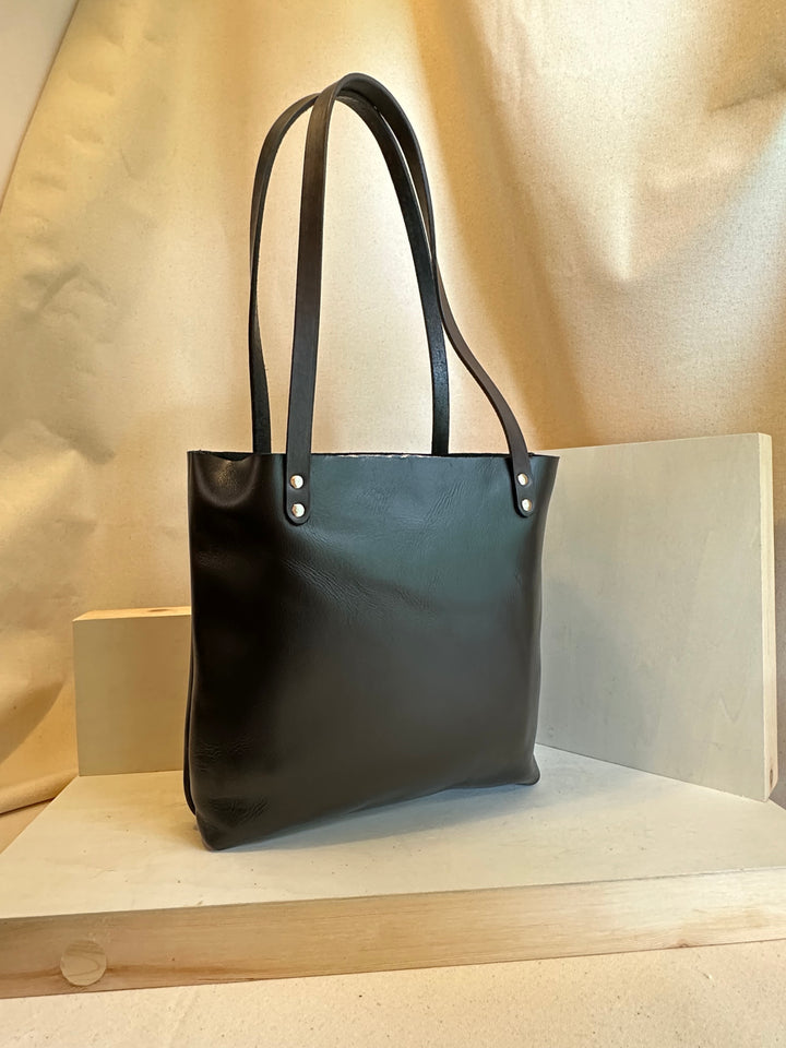 Our handmade Black Portfolio Leather Tote Bag is hand crafted in our Asheville, NC studio.   Made of the finest quality top grain Horween Chrome XL solid leather. It is our compact tote that can carry anything from top secret dossiers to mini bottles for apres-anything.  Made from the highest quality top grain, solid leather, this bag will outlast your sister's second and third marriages.  Black EDC Mini Leather Tote Bag