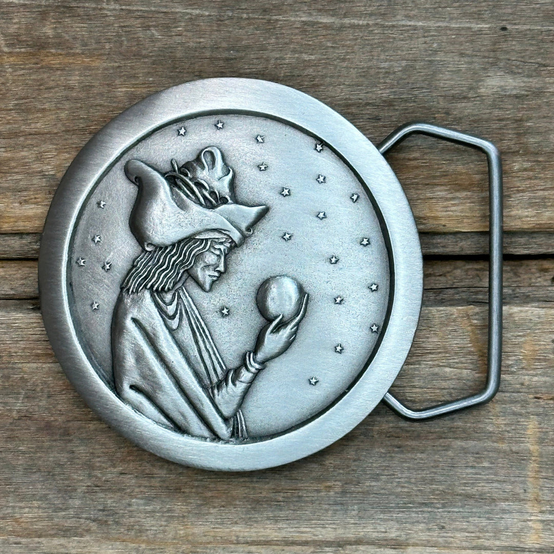 This is a pewter belt buckle with a silver tone.  It depicts merlin the wizard gazing into a crystal ball with tiny stars in the background.