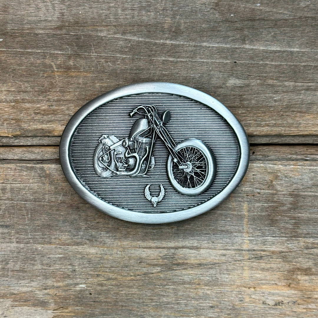 This is a pewter buckle with a silver tone.  It depicts a motorcycle with a tiny skull and cross bones below it.  This buckle is in the badass category.