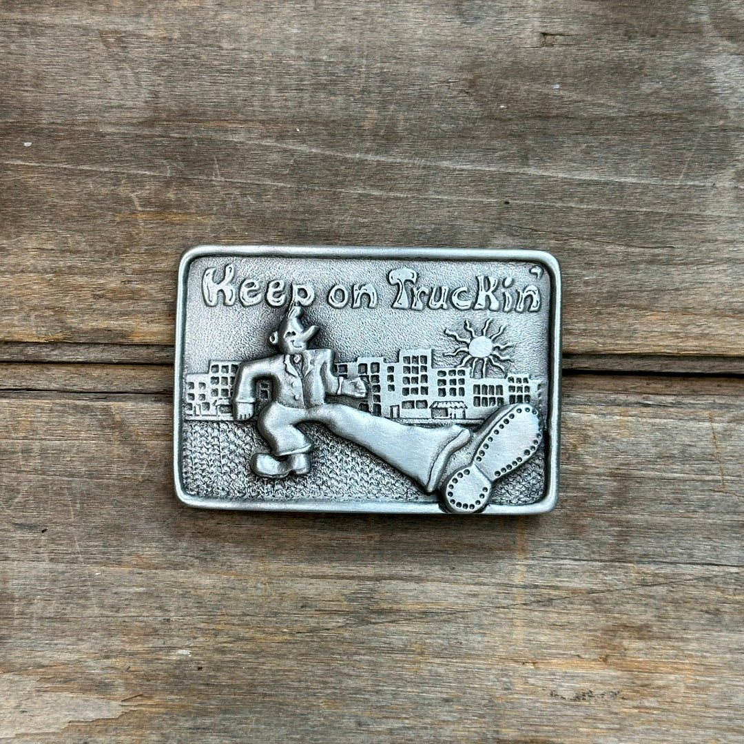 This is a pewter belt buclke with a silver tone.   It depicts an illustrated man with his leg extended, crossing the street.