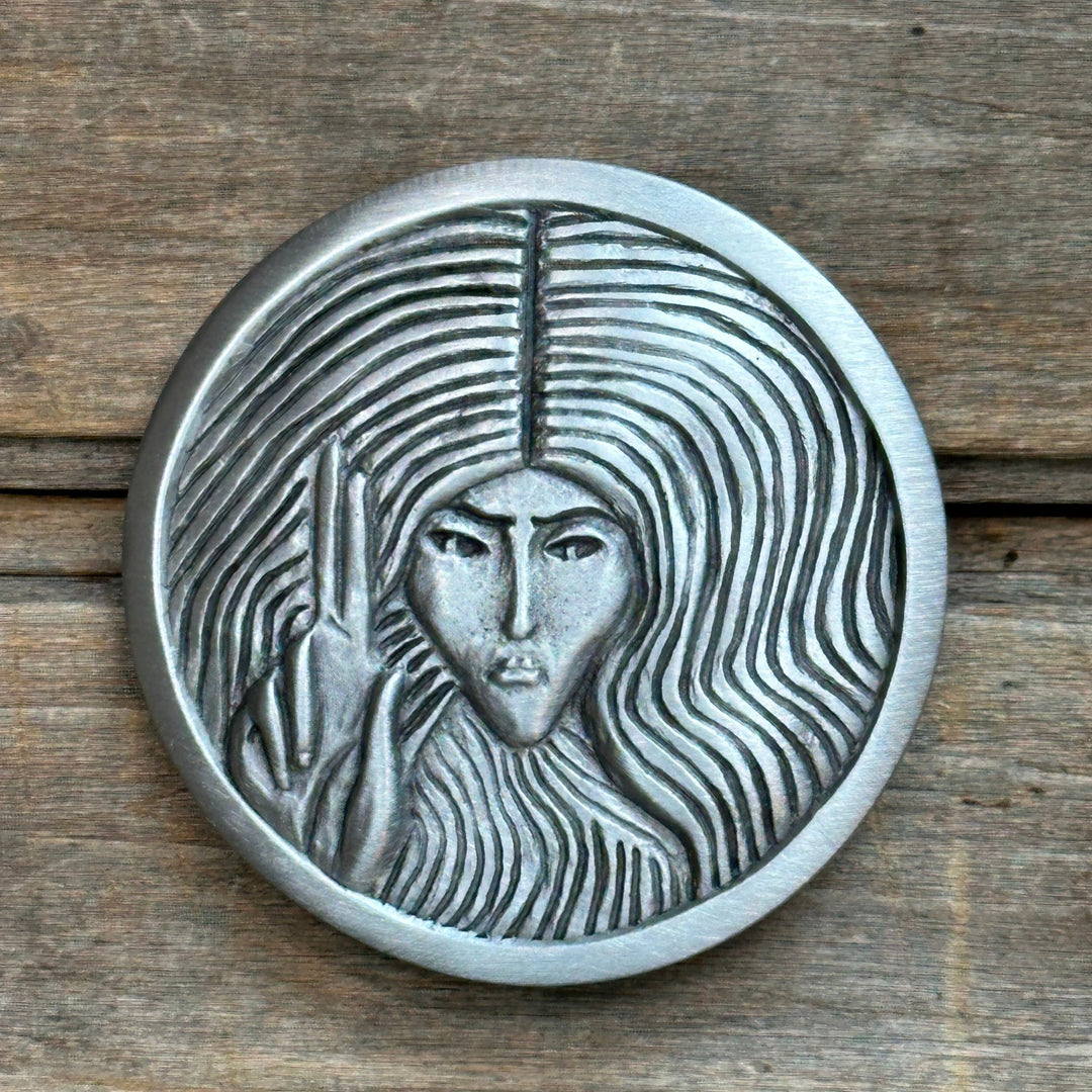 This is a pewter belt buckle with a silver tone.  It depicts a woman with her index and middle ifnger raised.  The design is inspired by an Audrey Beardsley illustration.