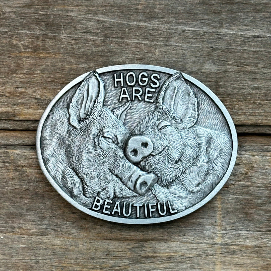 This is a pewter belt buckle with a silver tone.  It depicts two pigs nuzzling their snouts together.  It says "HOGS ARE BEAUTIFUL"
