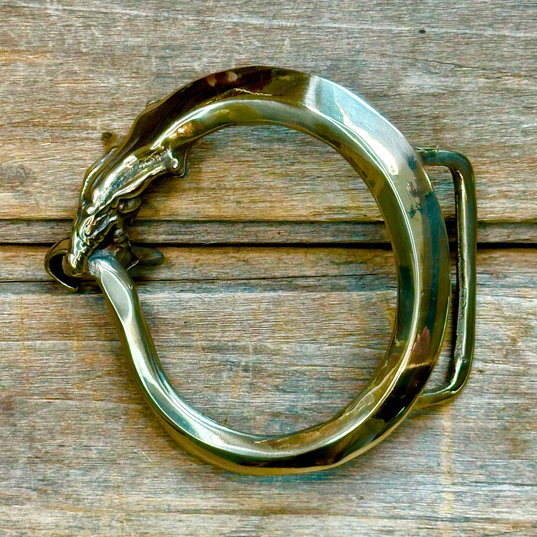 This is a solid brass belt buckle with a gold tone.  It depicts the Orobouros, a mythilogical serpent that eats its own tail, representing the cyclical nature of life.