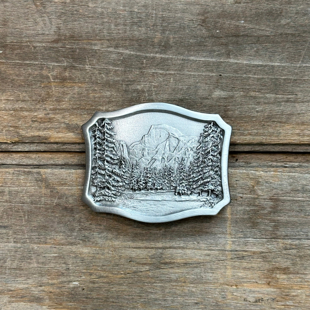 This is a pewter belt buckle with a silver tone.  It depicts the Yosemite half dome and trees along a stream.