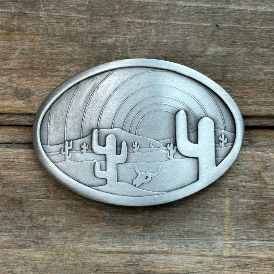 This is a pewter belt buckle that depicts a desert scene with cacti.  It has a silver tone.