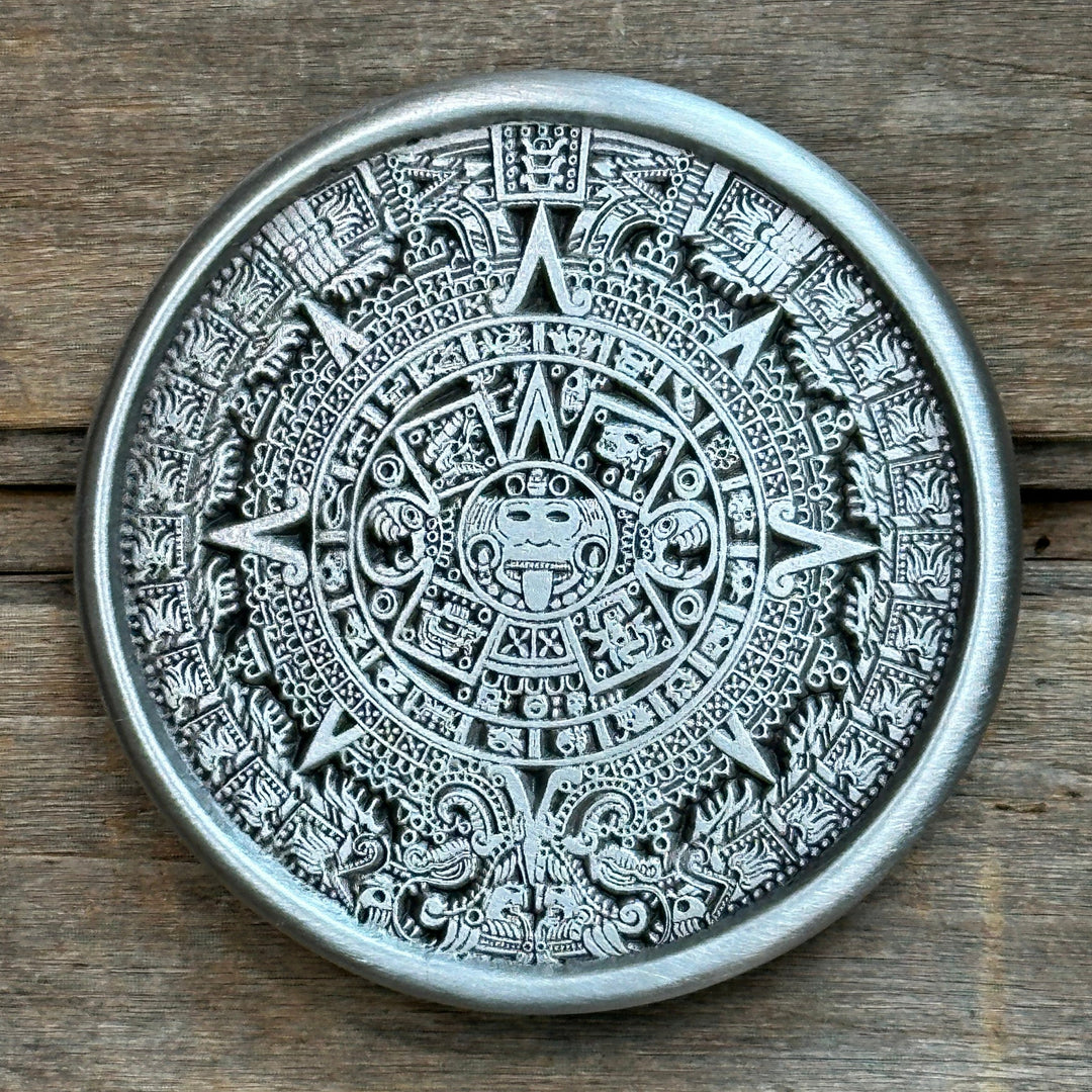This belt buckle depicts an Aztec calendar in great detail.  It is made of pewter, round, and silver in tone.