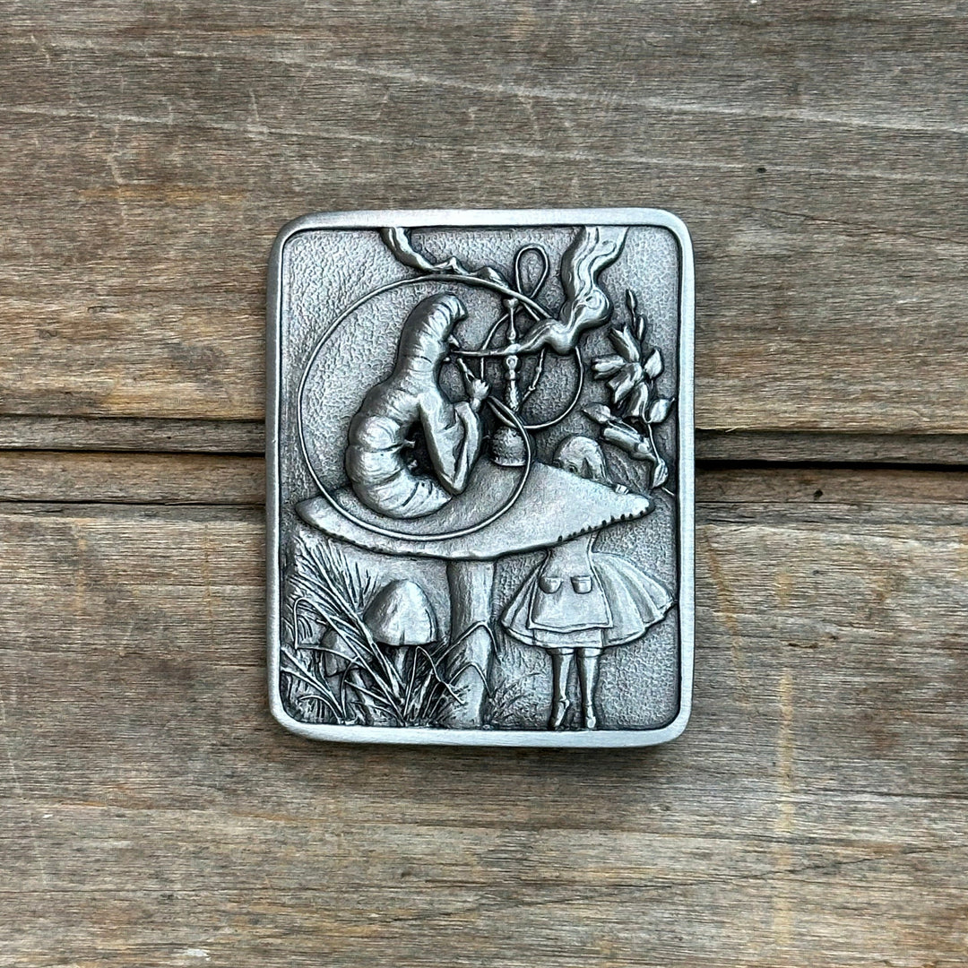 This belt buckle shows a scene from alice in wonderland when Alice talks to the hookah smoking caterpillar.  It is pewter and has a silver tone and fine details.